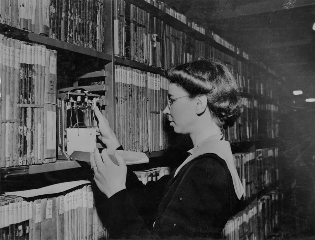 Archivist Adelaide Minogue inspecting a mechanical humidity recorder in library stacks on August 12, 1942