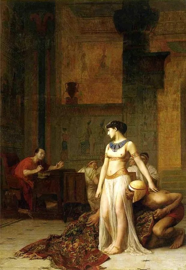 Cleopatra standing unrolled from fabric before a seated Julius Caesar in an Egyptian-columned interior, her servant Apollodorus crouching beside her