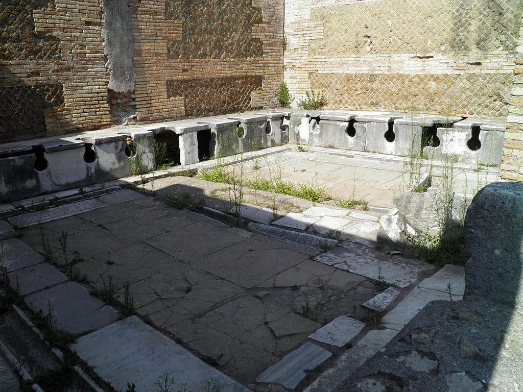 Roman public latrine forica at Ostia showing marble bench seating along three walls, World History Encyclopedia.