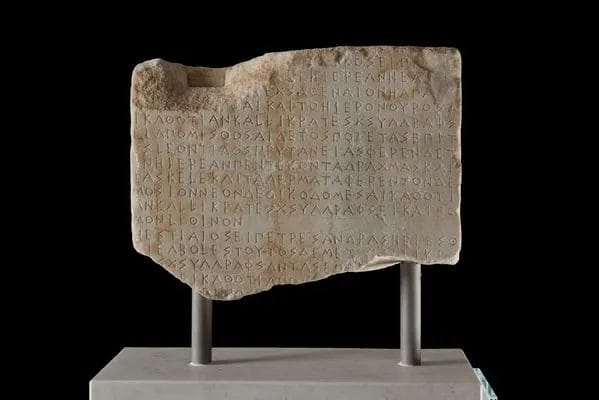 Pentelic marble inscription carved with ancient Greek text detailing ancient sacrifice temple regulations and priestess payments from the Athenian Acropolis.