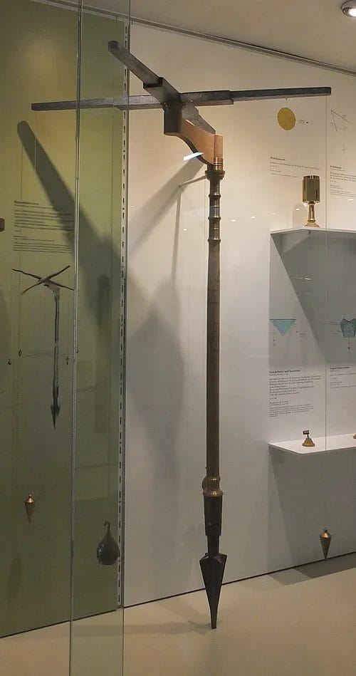 Groma reconstruction showing the stelletta cross with four hanging plumb bobs used in Roman surveying tools and methods.