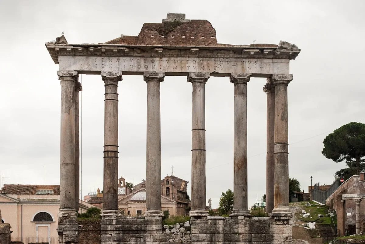 Temple of Saturn with eight tall columns standing against blue sky at base of Capitoline Hill
